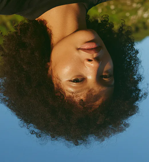 Close-up of a person with curly hair against a clear blue sky, image is upside down.