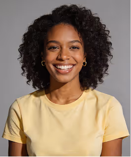 Smiling woman with curly hair wearing a yellow t-shirt and gold hoop earrings against a plain gray background.