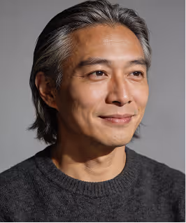 Middle-aged man with gray hair wearing a dark sweater, looking slightly to the side with a gentle smile.